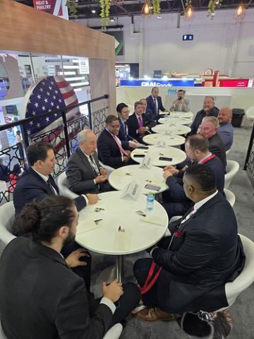 Administrator Daniel B. Whitley and U.S. Deputy Chief of Mission Eric Gaudiosi are seated at a table with members of the U.S. Meat Export Federation and Cooperators Program Division representatives Chris Jacquette and Zechariah Henderson. The group is engaged in discussion over a working lunch at Gulfood 2025. Plates of food, beverages, and trade materials are on the table